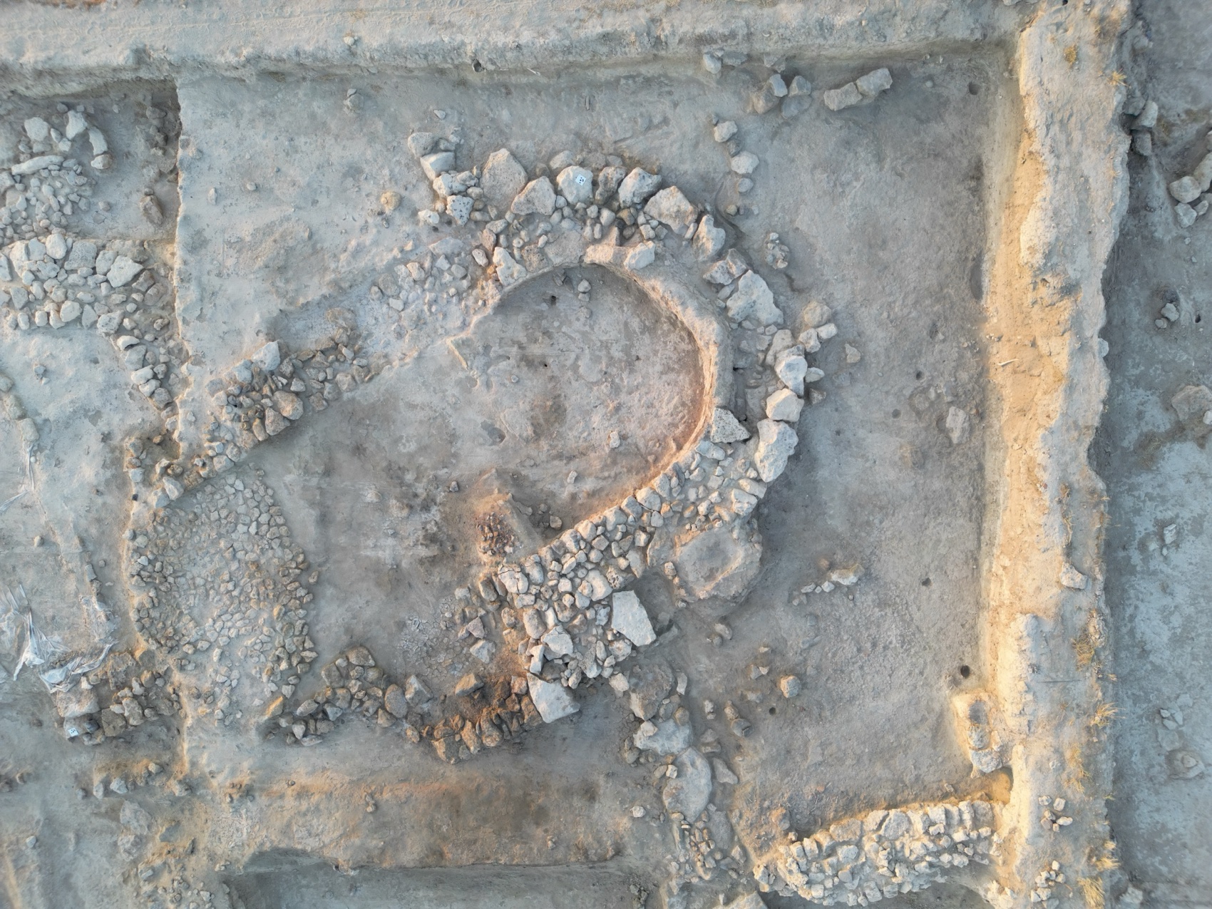 Overhead view: the stone walls of a horseshoe-plan apsidal building stand out in the raking light of sunset.