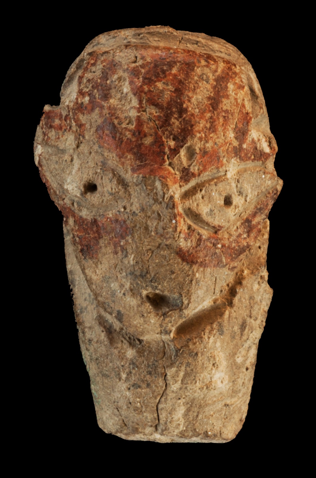 A clay human-head figurine against a dark background; modelled eyes and traces of red ochre on its surface.