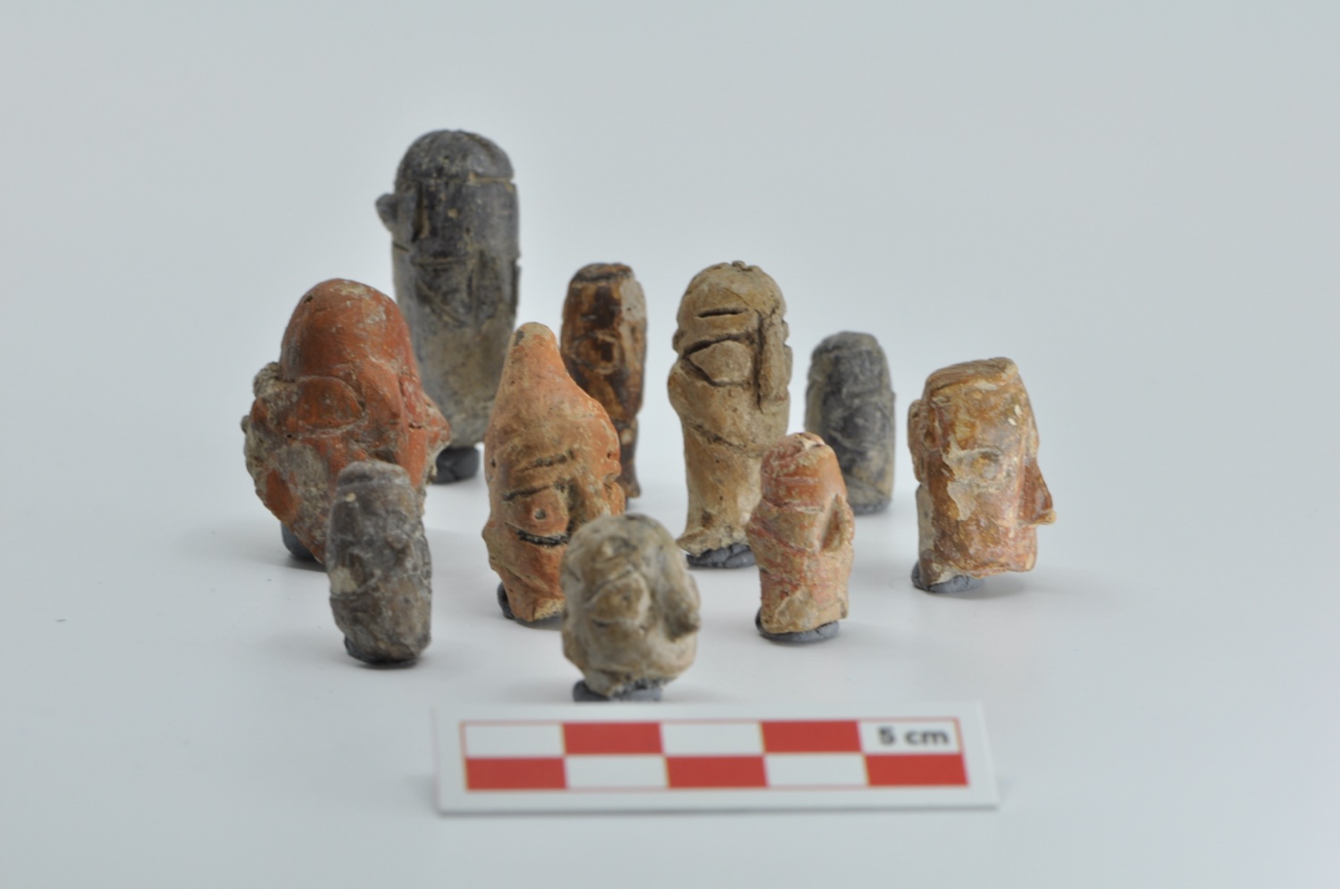 About ten small clay figurines together against a grey background, with a 5-centimetre scale in front.