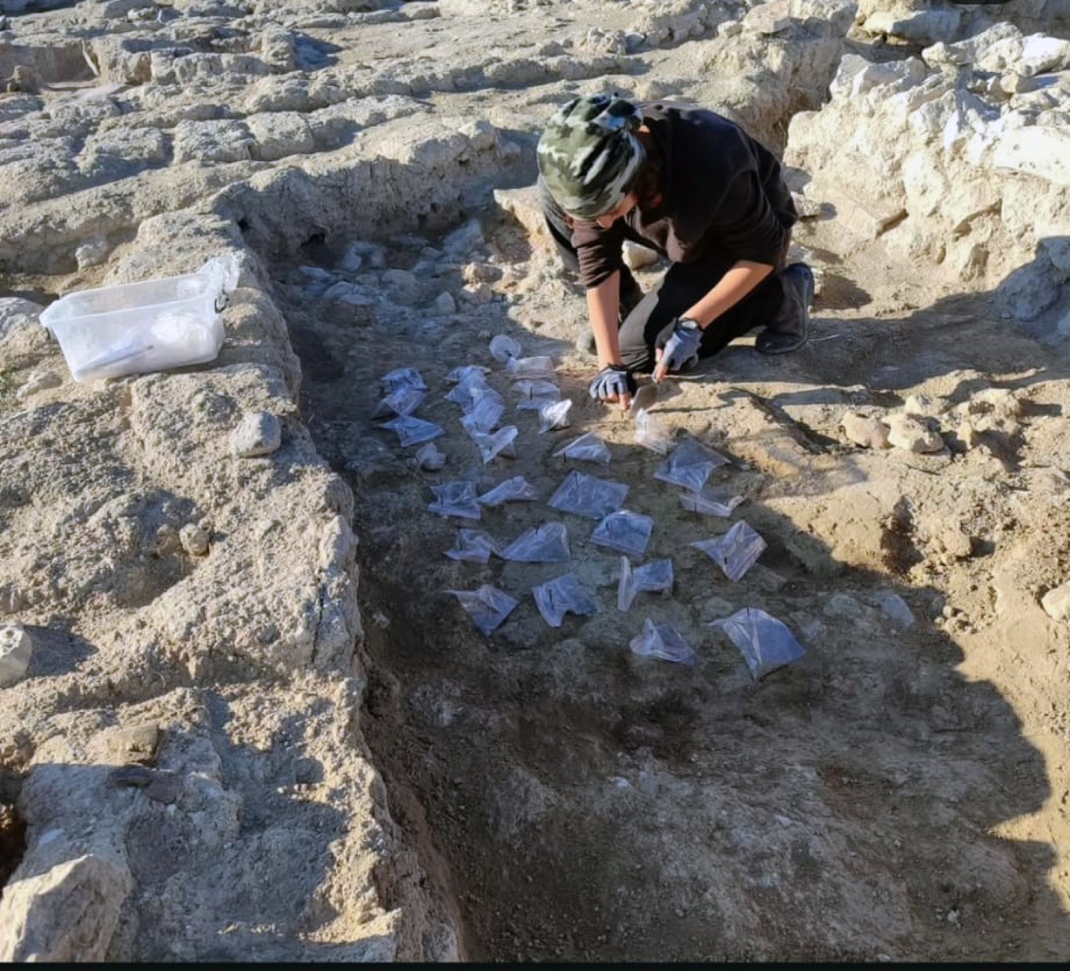A team member working over labelled bags of finds laid out in a trench.