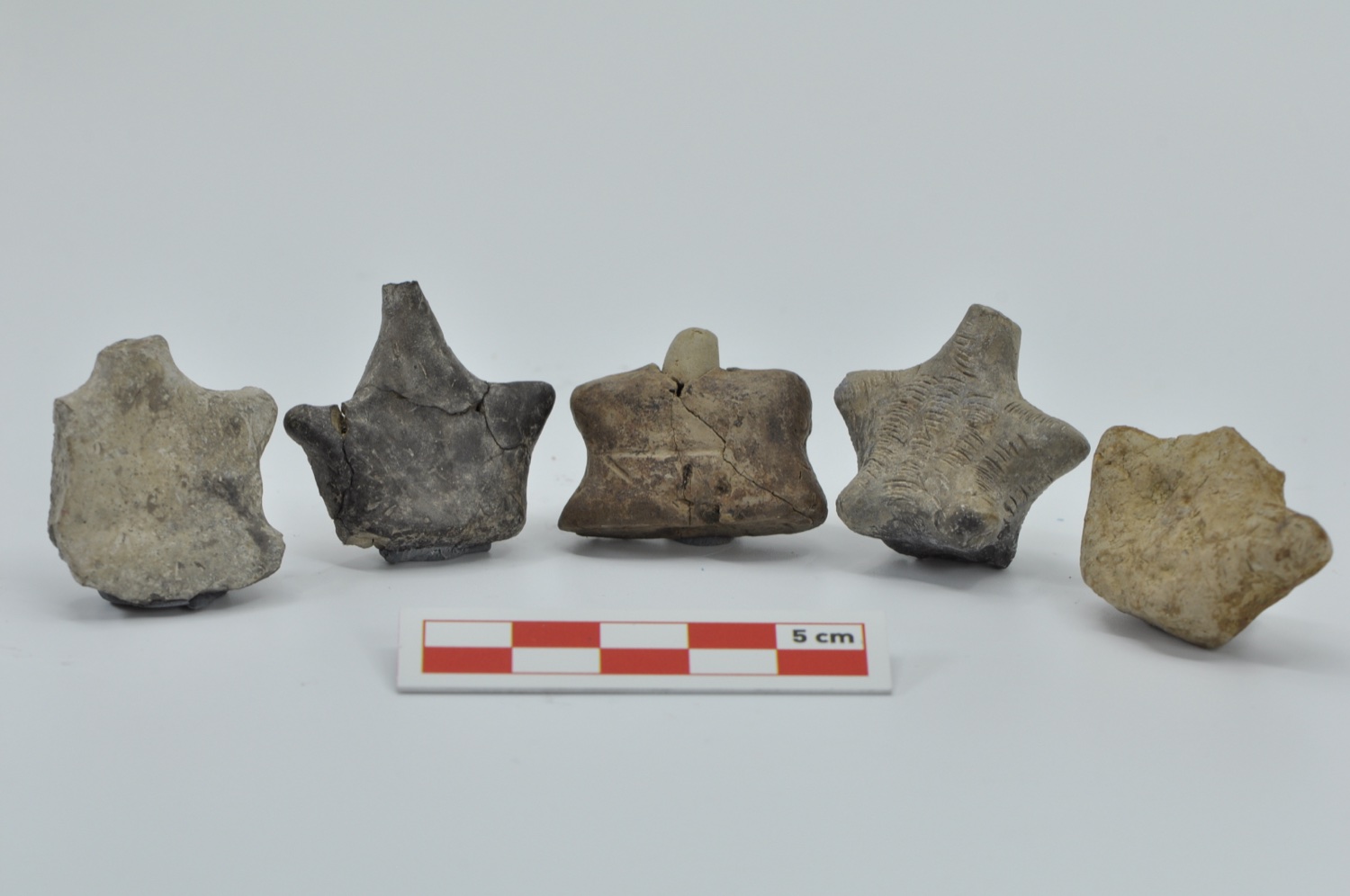 Five small clay objects against a grey background; impressed and incised decoration on their surfaces, with a scale in front.