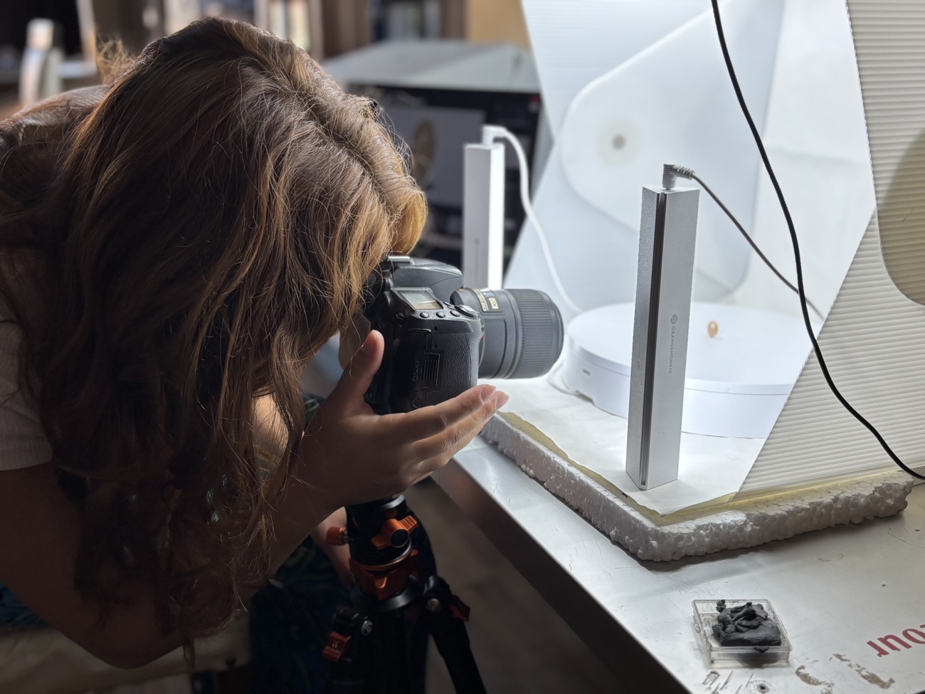 A team member photographing a small find on a tripod inside a light tent.